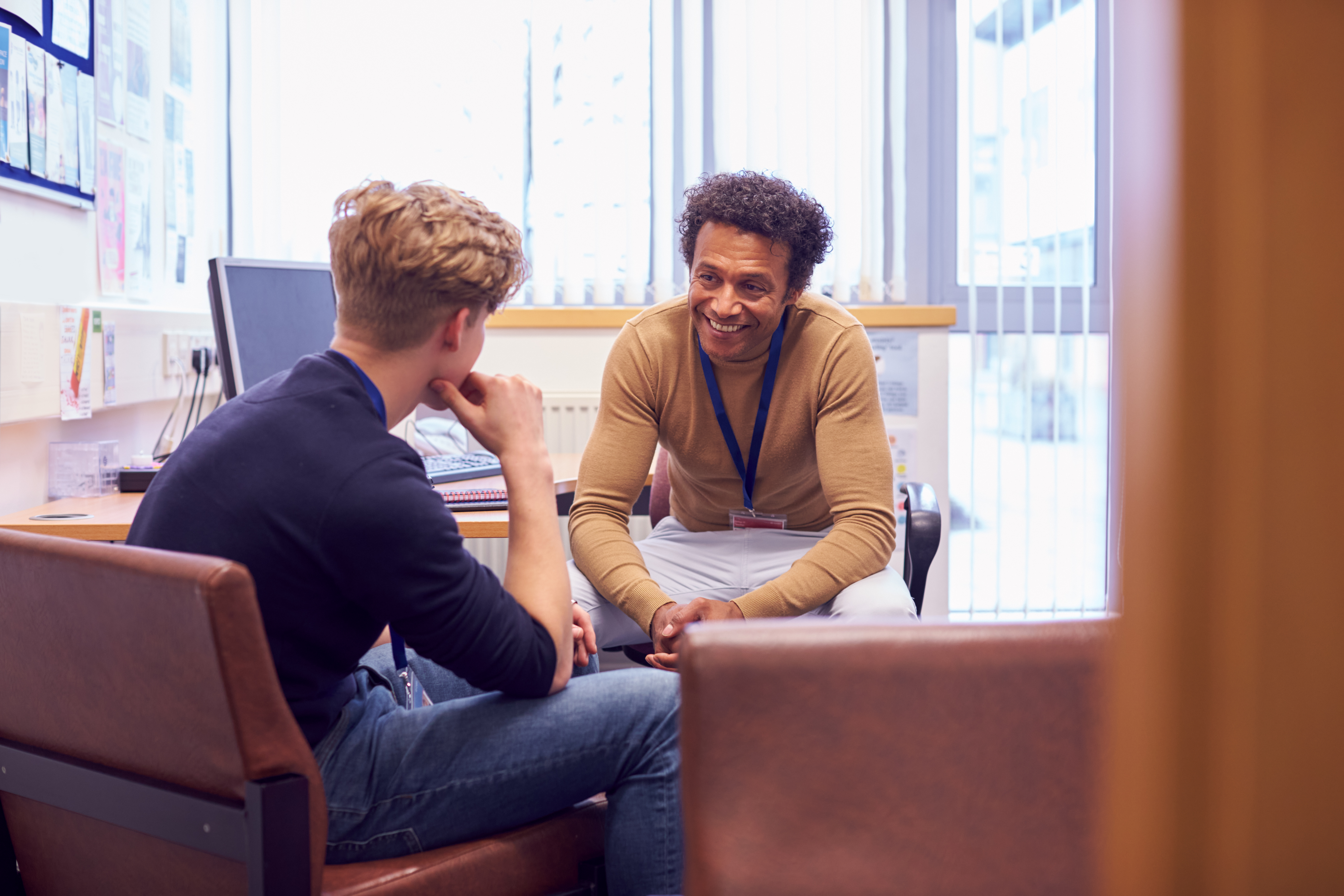 A school counselor smiles as he listens to a young male student speaking
