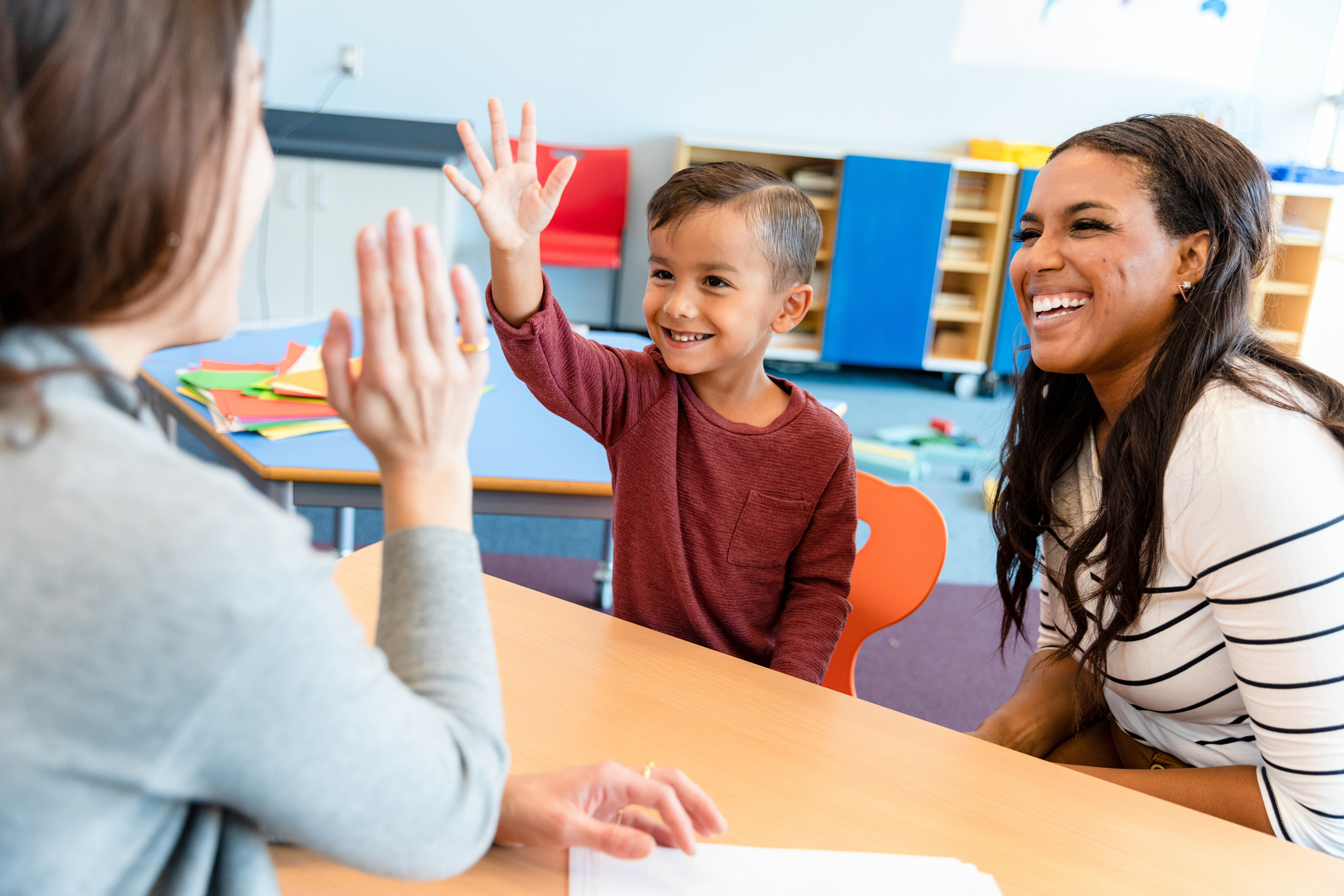 An educational therapist gives boy high five while mom smiles beside them