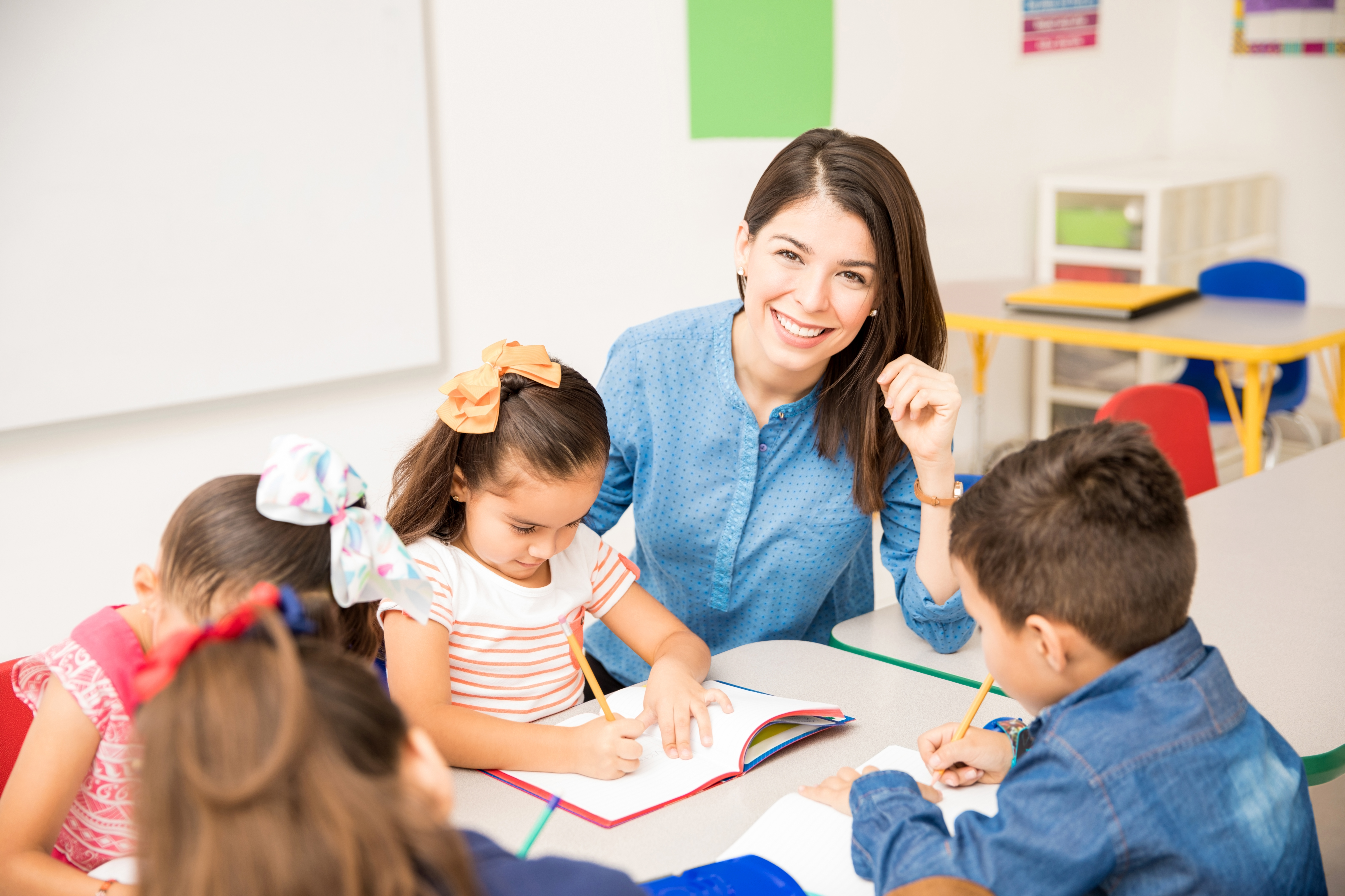 Hispanic female teacher seated at table with students smiling at the camera