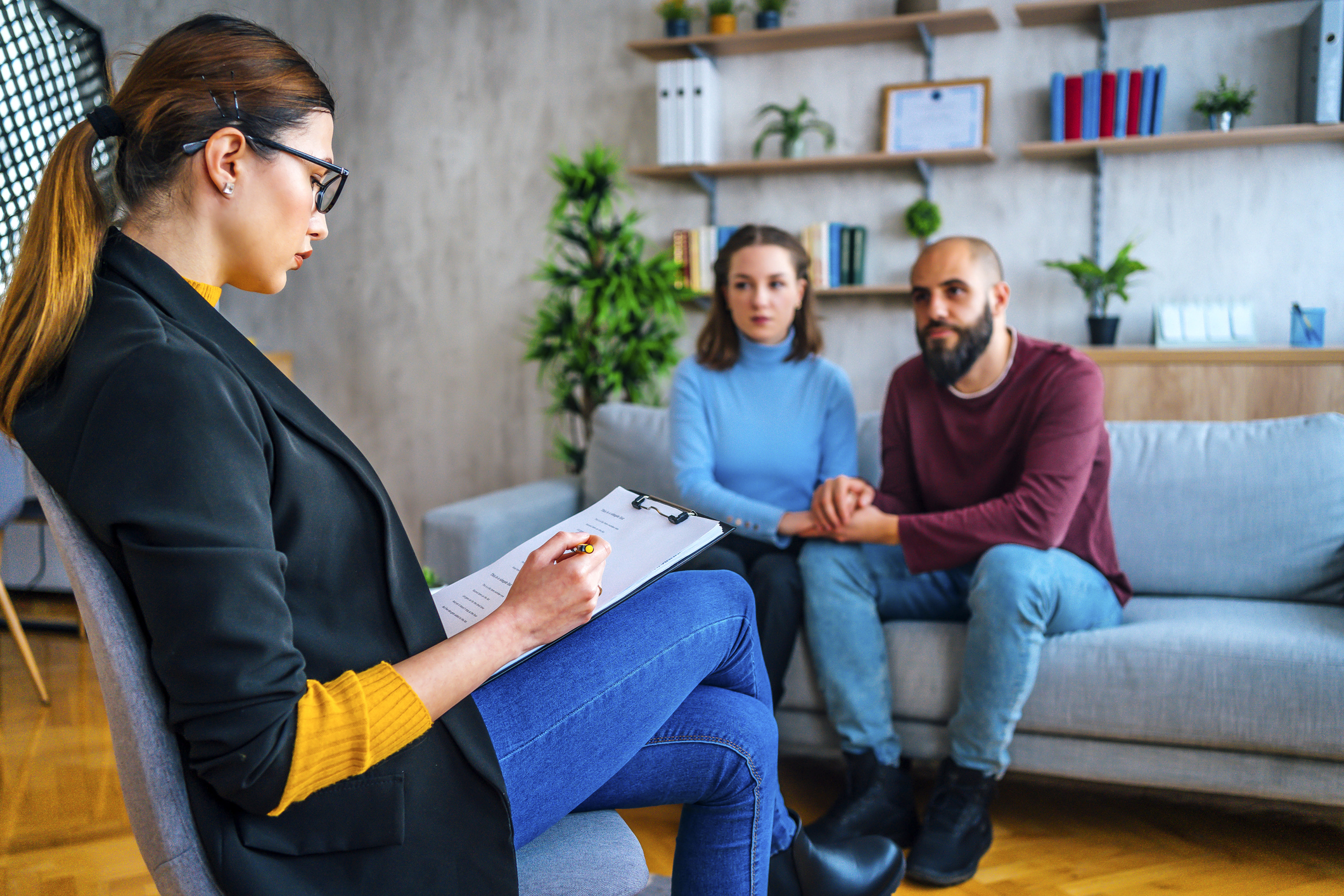A young female marriage and family therapist reviews her notes with couple seated on couch.