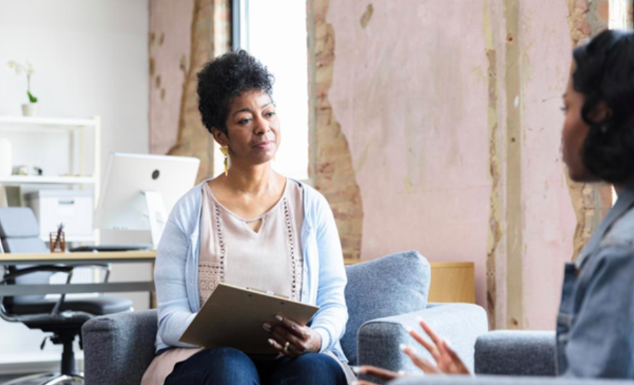 Mature Hispanic female therapist listens and takes notes in her office while her patient expresses themself