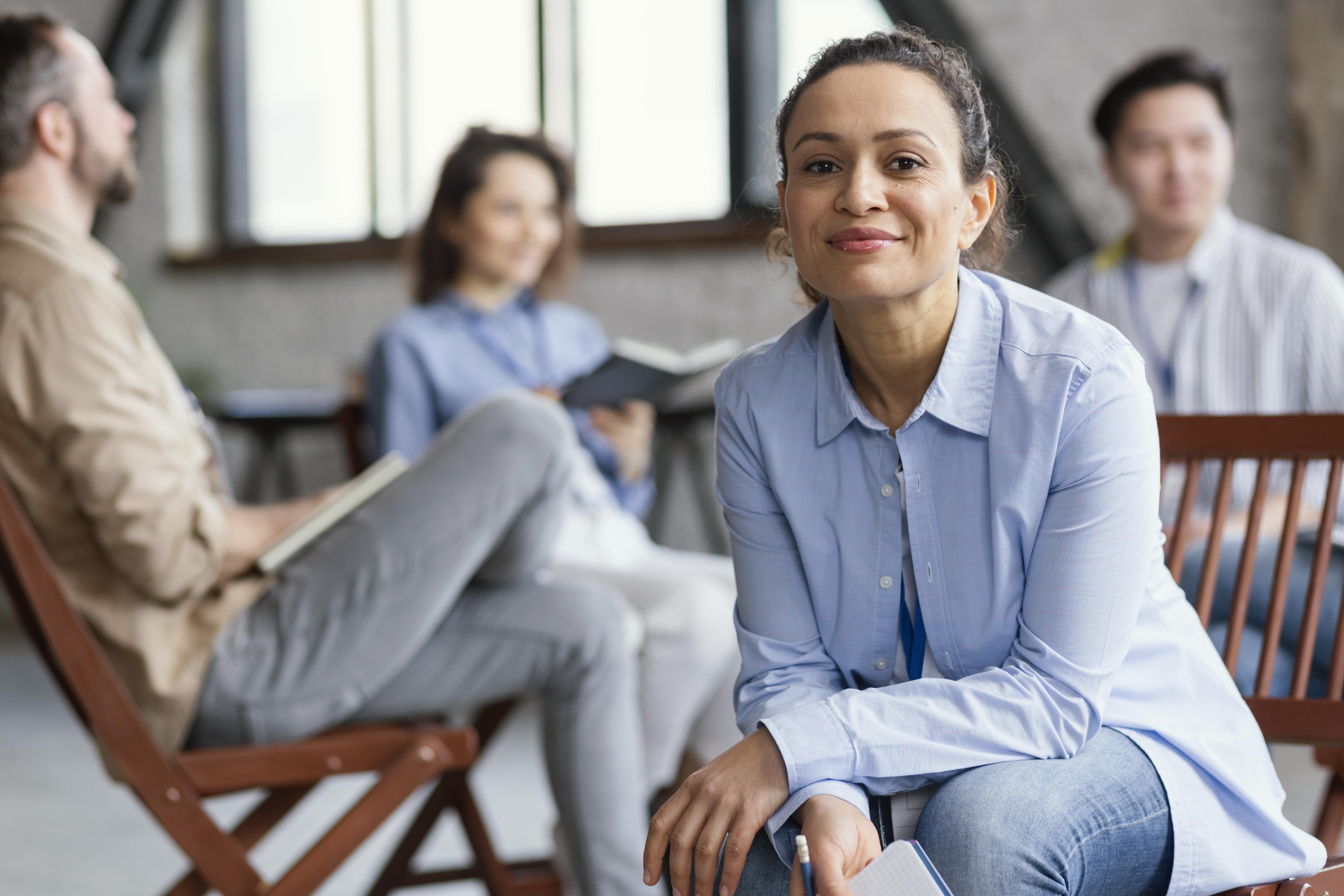 psychologist facing camera while group therapy session continues in background.jpg