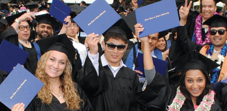 students in cap and gowns holding up diplomas